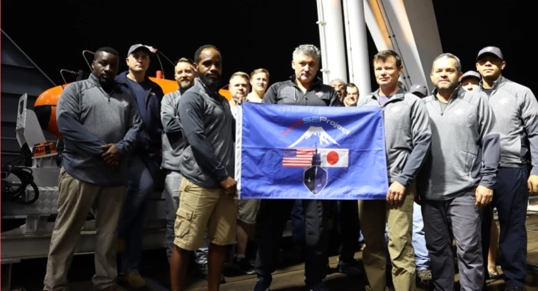 The 2022 discovery team on deck at night, holding a Lost 52 Project flag
